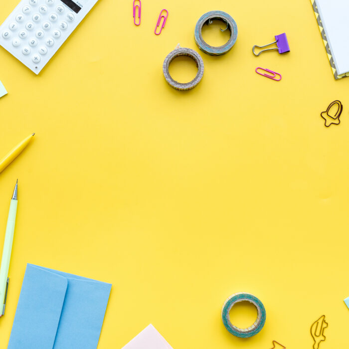Scattered stationery on student's desk. Yellow background top view.